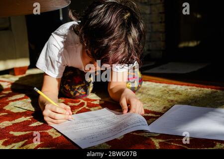 Un garçon se pose dans un tapis dans un patch lumineux de la lumière pour faire ses devoirs Banque D'Images