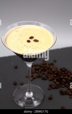 Un Martini expresso servi dans un verre de martini et garni de grains de café rôtis. Le verre est visible avec des grains de café fraîchement torréfiés. Banque D'Images