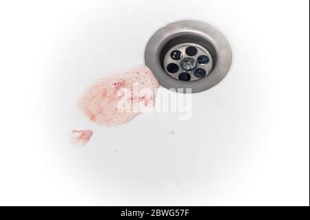 la salive avec du sang de gomme et du dentifrice après le brossage s'écoule dans le trou de vidange de l'évier Banque D'Images