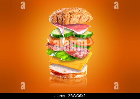 Sandwich savoureux volant. Sandwich avec des ingrédients volants isolés sur fond orange. Banque D'Images