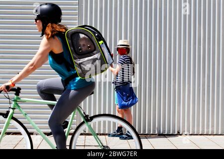 Un cycliste portant un chien sur son sac passe un garçon portant un masque rouge et un chapeau. Banque D'Images