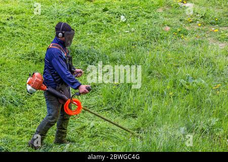 tondeuse homme avec tondeuse à ficelle et masque de visage trimmong herbe - gros plan Banque D'Images