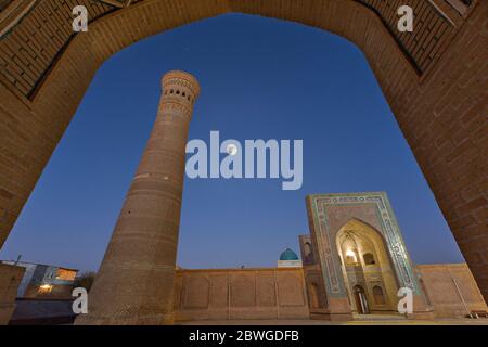 Vue sur la mosquée de POI Kalon et minaret à travers une arche avec la pleine lune dans le ciel, Boukhara, Ouzbékistan Banque D'Images