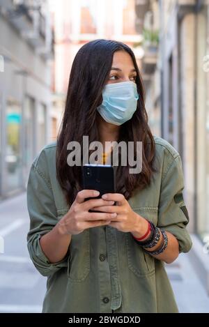 Femme portant un masque de protection sur son visage lorsqu'elle utilise un téléphone portable dans la rue Banque D'Images