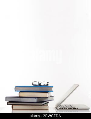 Concept d'apprentissage en ligne. Lunettes sur la pile de livres et un ordinateur portable isolé sur fond blanc. Éducation avec protection des yeux à distance. Photo verticale, Banque D'Images