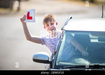 Un jeune conducteur apprenant qui célèbre son passage à l'essai routier en agitant ses plaques en L dans l'air. Banque D'Images