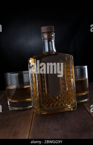 Deux verres avec alcool et une bouteille sur une table en bois dans une pièce sombre Banque D'Images