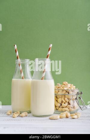 Deux bouteilles de lait de cajou végétarien avec noix de cajou sur fond vert Banque D'Images