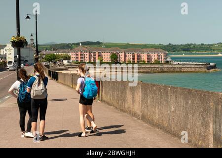 Groupe d'adolescents filles avec des sacs à dos accrochés autour de l'insouciance dans Lighthouse Hill Street l'après-midi ensoleillé d'été à Youghal, comté de Cork, Irlande Banque D'Images