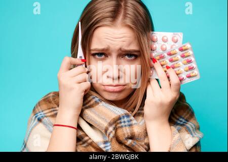 Femme bouleversée avec thermomètre et pilules enveloppées dans le plat. La femme est malade et a de la fièvre Banque D'Images