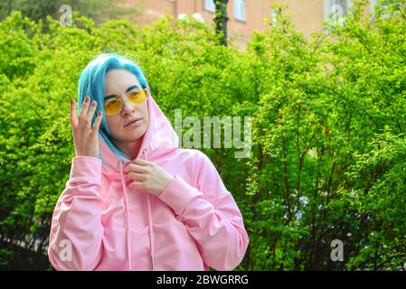 Portrait de jeune femme avec cheveux bleus et lunettes de soleil stylées sur la rue de la ville en journée ensoleillée Banque D'Images