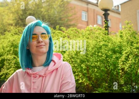 Portrait de la femme heureuse avec des cheveux bleus et des lunettes de soleil stylées sur la rue de la ville en journée ensoleillée Banque D'Images