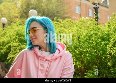 Portrait de jeune femme avec cheveux bleus et lunettes de soleil stylées sur la rue de la ville en journée ensoleillée Banque D'Images