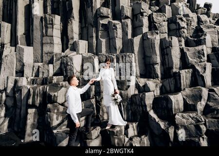 Un couple de mariage se dresse sur un mur de piliers en pierre. La mariée et le marié s'embrassent sur basalte Kekurs, sur la plage de sable noir de Vik. Destination Banque D'Images
