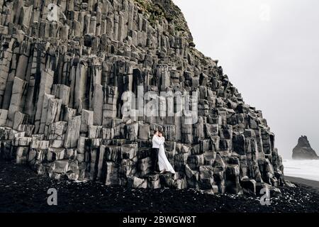 Un couple de mariage se dresse sur un mur de piliers en pierre. La mariée et le marié s'embrassent sur basalte Kekurs, sur la plage de sable noir de Vik. Destination Banque D'Images