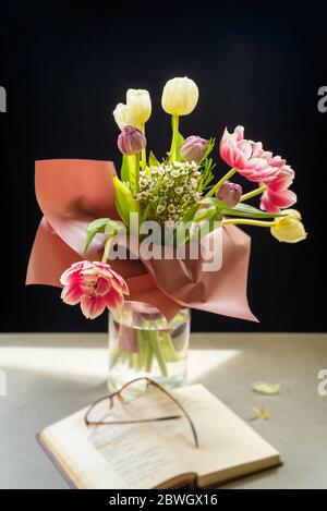 Gros plan d'un bouquet de fleurs printanières sur une table à côté d'un livre ouvert, de verres, de focus sélectif Banque D'Images