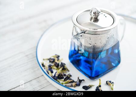 Théière en verre avec thé Anchan bleu sur fond de bois blanc, vue du dessus Banque D'Images