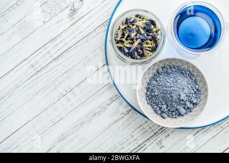 Thé bleu biologique Anchan, Clitoria, papillon Pea en verre avec fleurs de Clitoria séchées et poudre de matcha bleue sur fond de bois blanc, vue du dessus Banque D'Images