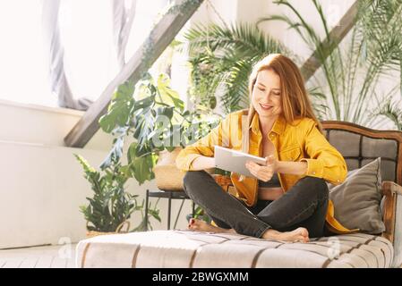 Une jeune femme magnifique est assise sur Internet dans son jardin sur une tablette. La fille recherche sur Internet des informations sur les plantes et joue gam Banque D'Images