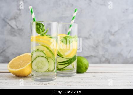 Eau perfusée avec concombre, citron, lime et basilic dans du verre sur fond gris Banque D'Images