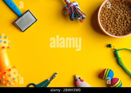 Composition de la couche plate avec accessoires pour animaux et bol d'aliments secs sur fond jaune. Concept de soin et de formation des animaux. Banque D'Images