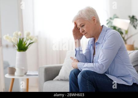 Femme climax. Portrait d'une femme âgée déprimée assise sur un canapé à la maison Banque D'Images