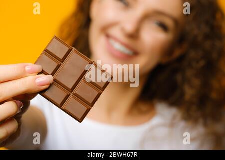 Gros plan de la barre de chocolat au lait sucré dans les mains d'une adolescente isolée sur fond jaune en studio Banque D'Images