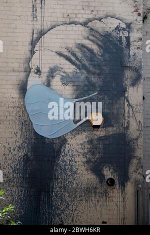 Un graffiti de style Banksy de la 'fille avec une perle Earring' par Vermeer, avec un masque chirurgical, fait de tissu, en utilisant un boîtier d'alarme pour les boucles d'oreilles. Banque D'Images