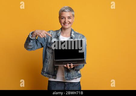Sites Web indépendants. Femme d'âge moyen positive pointant vers un ordinateur portable avec écran noir Banque D'Images