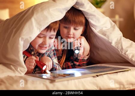 Les petits enfants lisent le livre sous couverture la nuit Banque D'Images