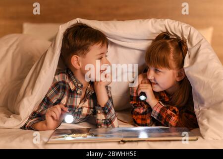 Les petits enfants lisent le livre sous couverture la nuit Banque D'Images