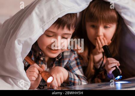 Les petits enfants lisent le livre sous couverture la nuit Banque D'Images