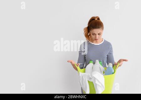 Femme troublée avec un linge propre et des détergents sur fond blanc Banque D'Images