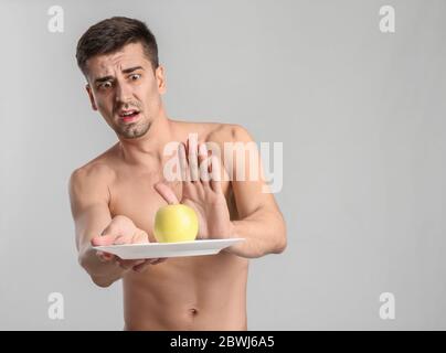 Homme effrayé avec pomme sur fond gris. Concept d'anorexie Banque D'Images