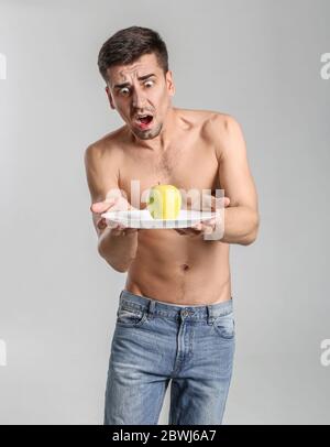 Homme effrayé avec pomme sur fond gris. Concept d'anorexie Banque D'Images