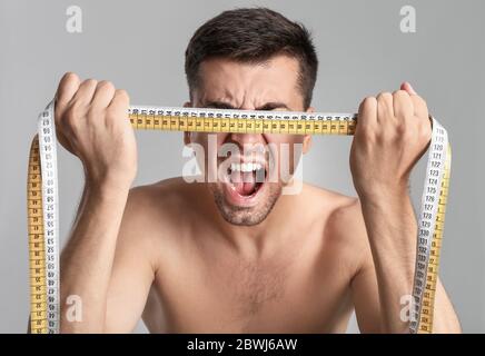 Hurler homme avec des rubans de mesure sur fond gris. Concept d'anorexie Banque D'Images