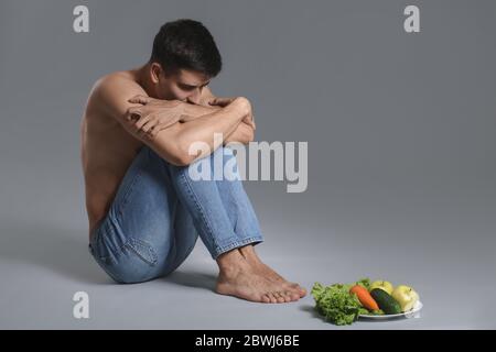 Homme malade avec des légumes frais sur fond gris. Concept d'anorexie Banque D'Images