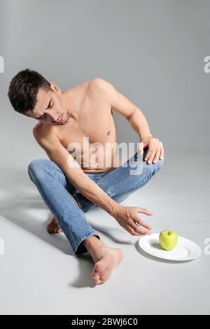 Homme malade avec pomme sur fond gris. Concept d'anorexie Banque D'Images