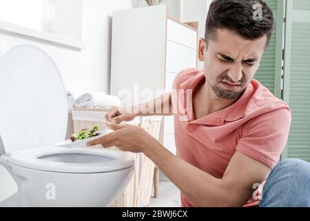 Un homme mécontent souffrant d'anorexie près d'un bol de toilettes avec salade sur l'assiette Banque D'Images
