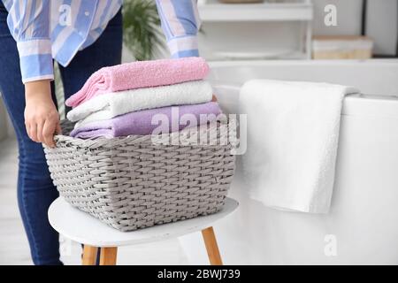 Femme mettant le panier avec du linge propre sur un tabouret dans la salle de bains Banque D'Images