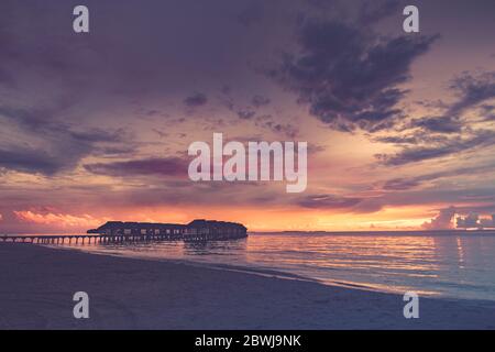 Coucher de soleil sur l'île des Maldives, complexe de villas aquatiques. Ciel et nuages magnifiques. Magnifique fond de plage pour les voyages d'été avec soleil, jetée en bois de plage Banque D'Images