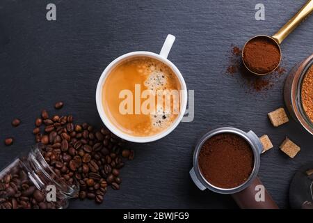 Vue de dessus d'une tasse d'espresso, de grains de café, de mouture et de sucre sur une table en pierre noire. Banque D'Images