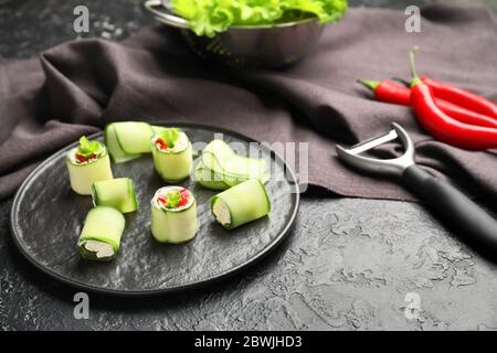 Assiette avec de savoureux rouleaux de concombre sur fond sombre Banque D'Images
