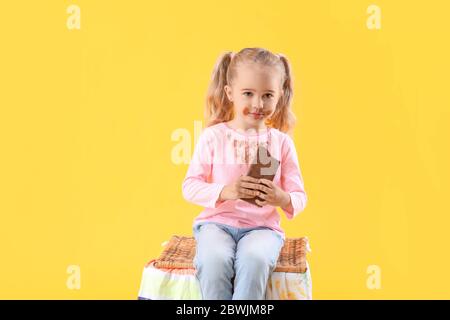 Petite fille dans des vêtements sales manger du chocolat sur fond de couleur Banque D'Images