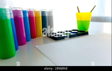 Papier blanc avec plusieurs contenants de peinture acrylique et une tasse en plastique avec de l'eau et des brosses à l'intérieur Banque D'Images