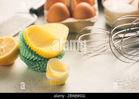 Muffins les tasses à pâtisserie avec les produits et les ustensiles sur fond clair Banque D'Images