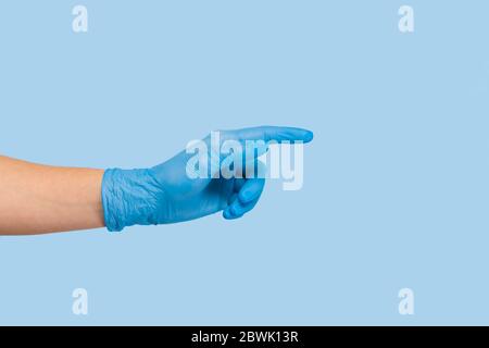 La main d'un médecin dans un gant médical bleu pointe vers un espace vide sur fond bleu. Banque D'Images