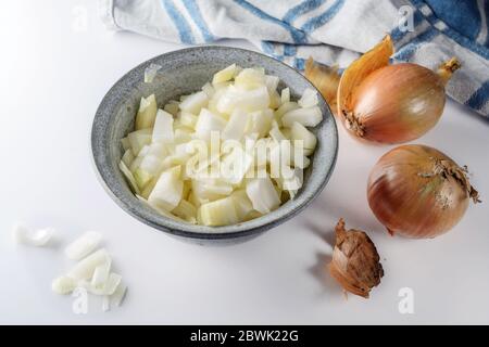 Oignons grossièrement hachés dans un bol et oignons entiers à côté sur une table blanche avec une serviette de cuisine bleue, concept de cuisine maison, foyer sélectionné Banque D'Images
