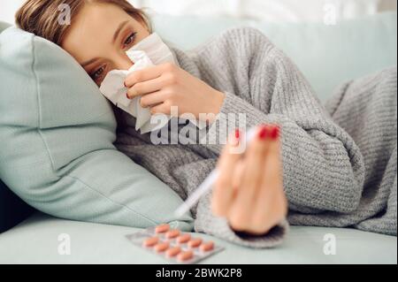 Malade de la femme caucasienne utilisant du papier de tissu sur le lit avec un thermomètre et des pilules Banque D'Images