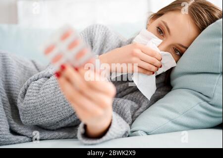 Femme malade utilisant le papier de soie et de pilules de maintien. Grippe. Éternuer dans le mouchoir. Maux de tête. Virus .médicaments. Femelle infectée, nez soufflant. Fille avec Banque D'Images